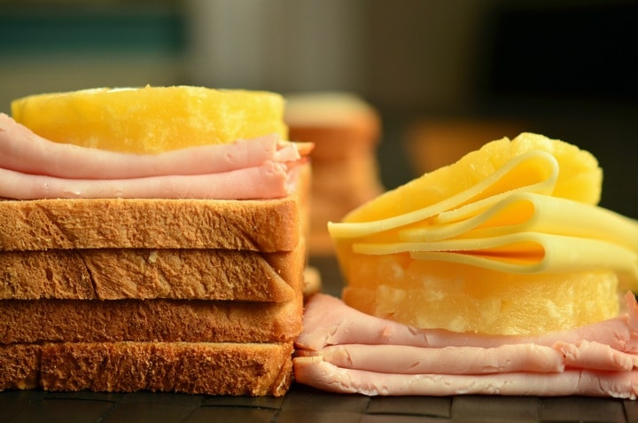 Bílé plátky chleba servírované na sobě se šunkou a sýrem.