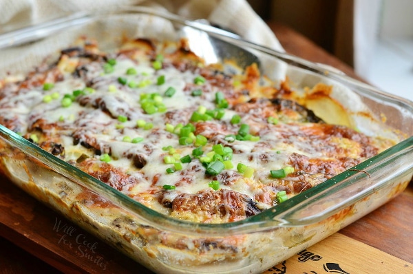 Baked potatoes with mushrooms and cheese sprinkled with spring onions in a baking dish.