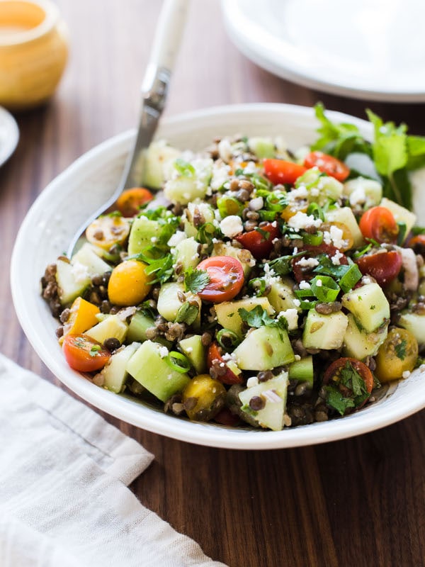Salada de lentilha, legumes frescos, ervas e molho servido em prato fundo com colher.