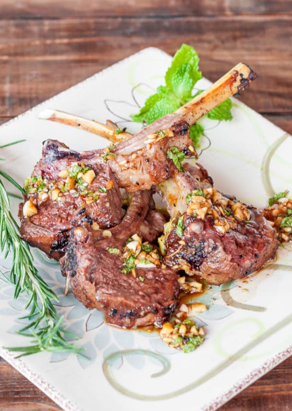 Lamb chops baked with bacon, onion, garlic and rosemary, served on a plate with fresh herbs.