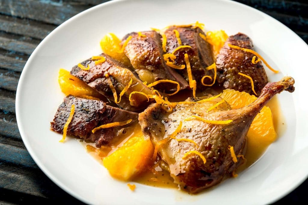 Sliced duck served with oranges on a plate.