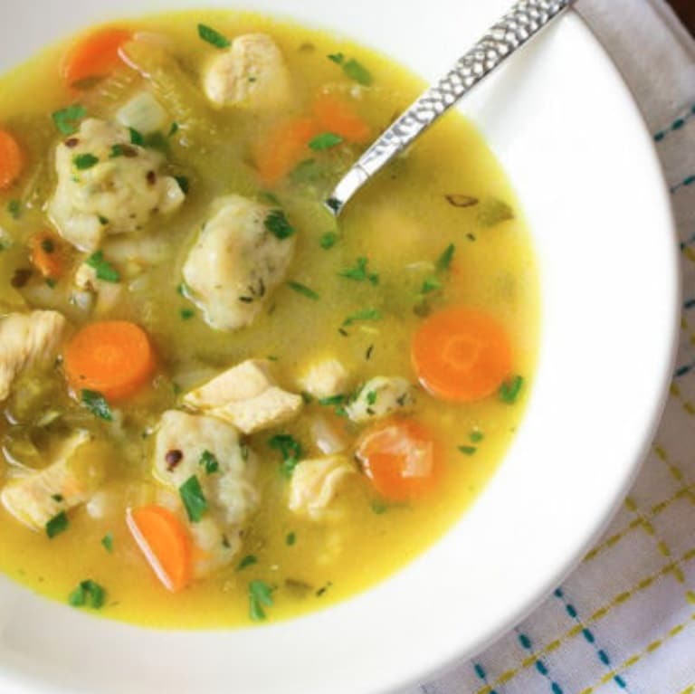 Polévka z ryby a zeleniny servírovaná v hlubokém talíři se lžící.