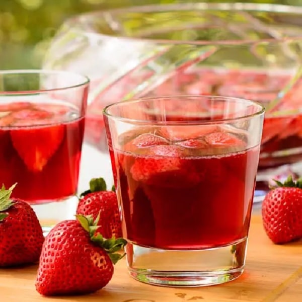 Erdbeerwein in Gläsern mit frischen Erdbeeren daneben.
