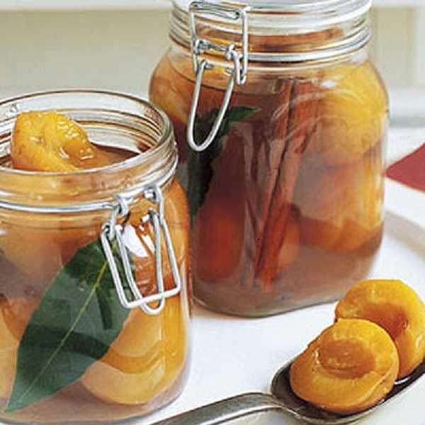 Apricots pickled in alcohol in glasses with a spoon of apricots placed next to it.