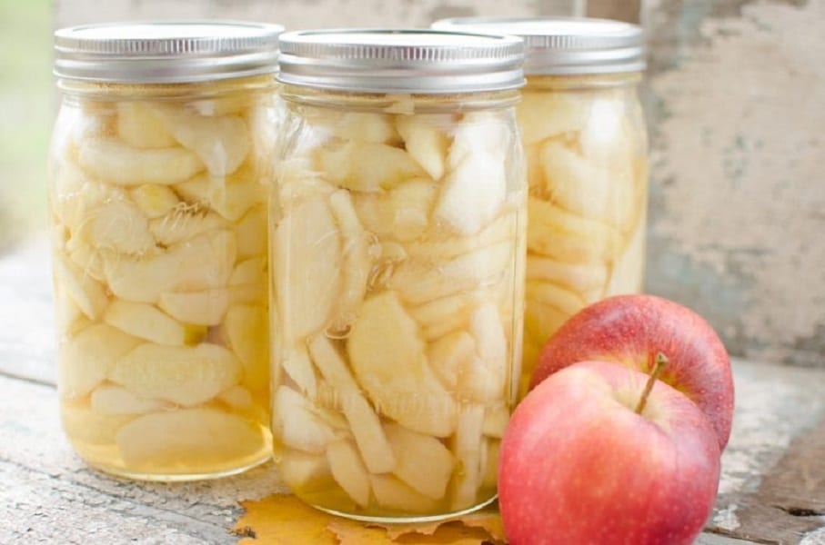Nakládaná jablka v zavařovacích sklenicích a vedle položená čerstvá jablka.