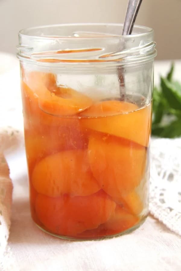 Pickled apricots in a jar with a spoon.