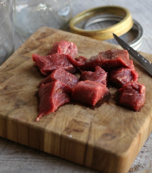 Kostky syrového masa na dřevěném prkénku s nožem.