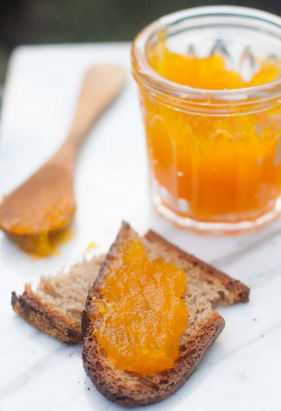 Pumpkin jam in a glass, a wooden spoon and the edges of bread smeared with jam.