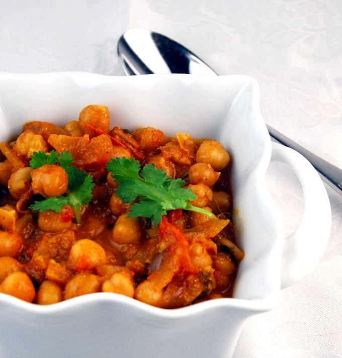 Indian chickpeas in a deep plate, decorated with herbs with a spoon placed next to it.