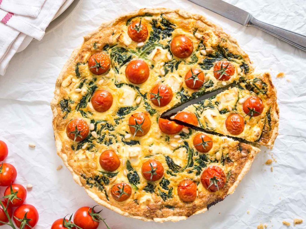 round savory pie with whole cherry tomatoes with pieces of spinach