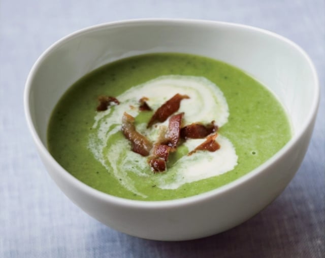 Pea soup with bacon, garnished with cream, in a white bowl.