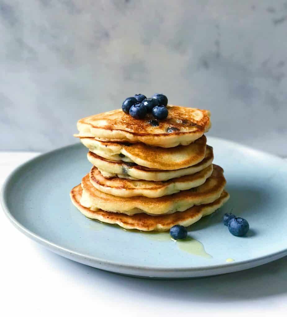 Fried pancakes with kefir, stacked on top of each other on a plate and decorated with fresh blueberries.