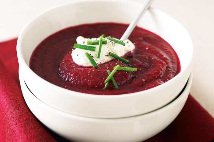 Creamy beetroot soup in a white bowl, garnished with cream and chives.