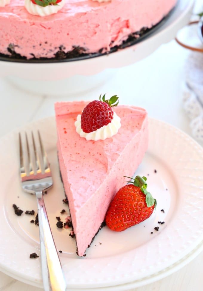Portion of strawberry cake with whipped cream meringue and fresh strawberry on a plate with a fork