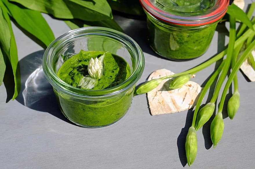 Two glasses of pesto with flowers and leaves of wild garlic