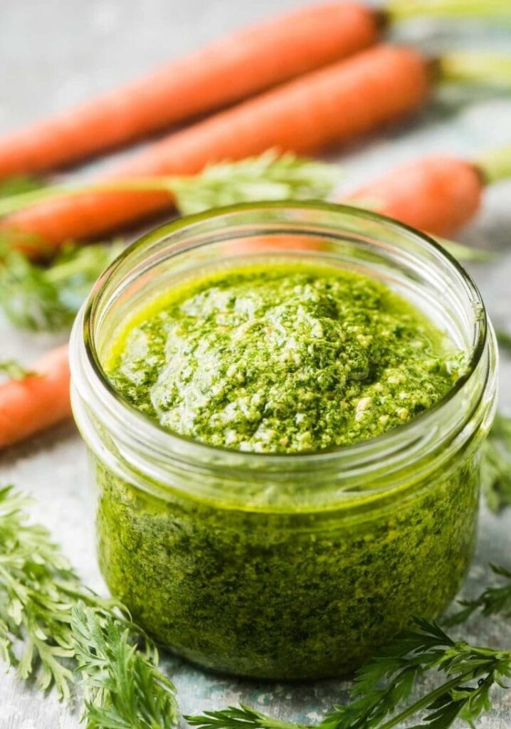 A glass jar with pesto lined with carrots and carrot filling