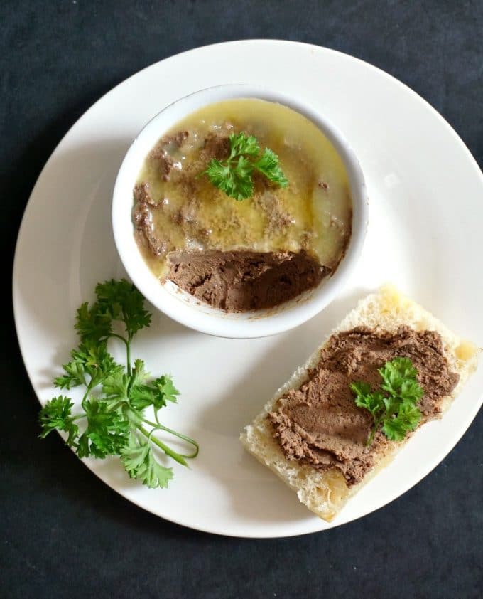 Homemade liver pate decorated with parsley in a baking dish and spread on a baguette