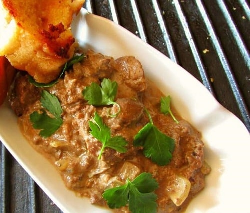 Pieces of liver in a cream sauce, garnished with fresh parsley and served with pastries.