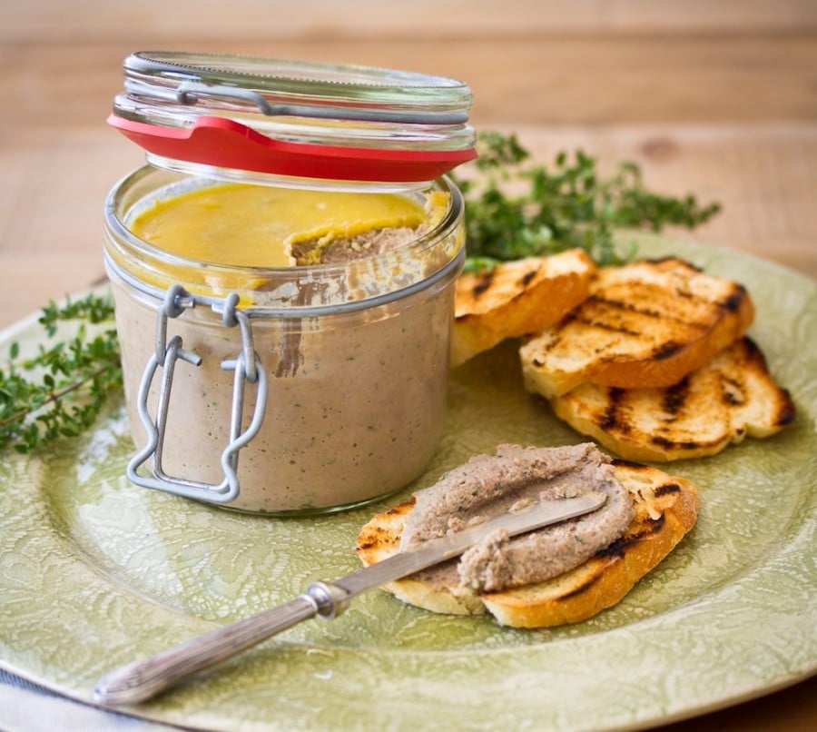 Pate spread on a slice of toasted bread and a glass with homemade meat spread