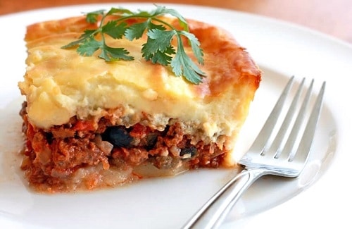 Baked minced meat with eggplant and béchamel, garnished with parsley.