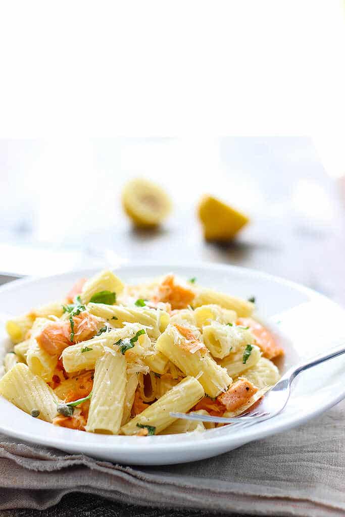 Rigatoni with salmon and parmesan with a fork on a white plate.
