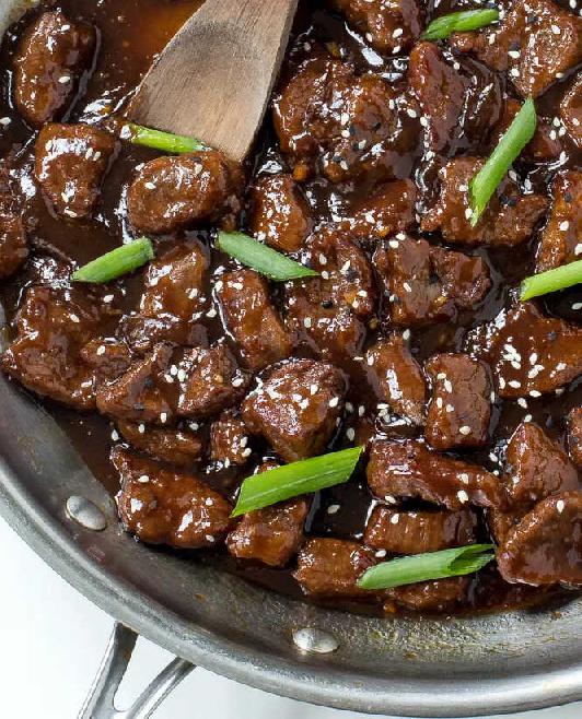 Mongolian beef with spring onions in a pan with a wooden spoon.