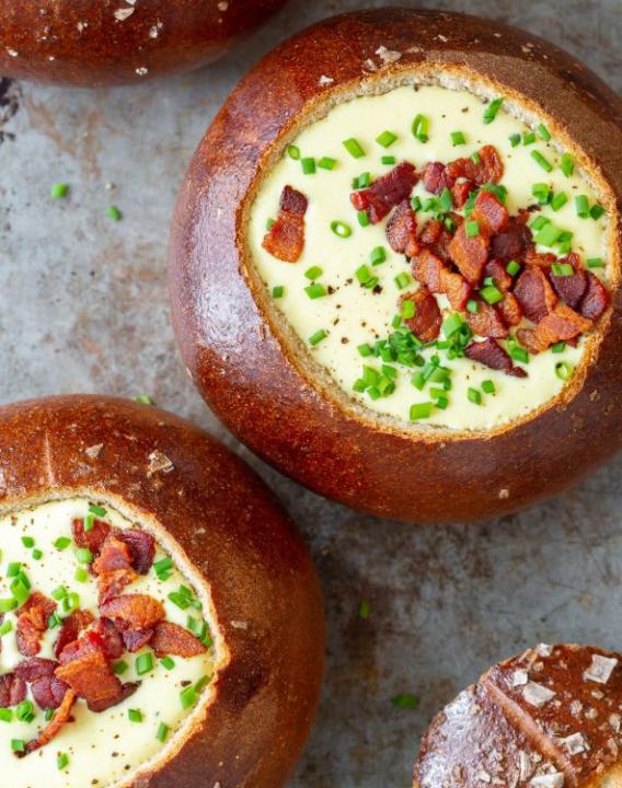 Bread bowls filled with cheese cream decorated with pieces of fried bacon and chives