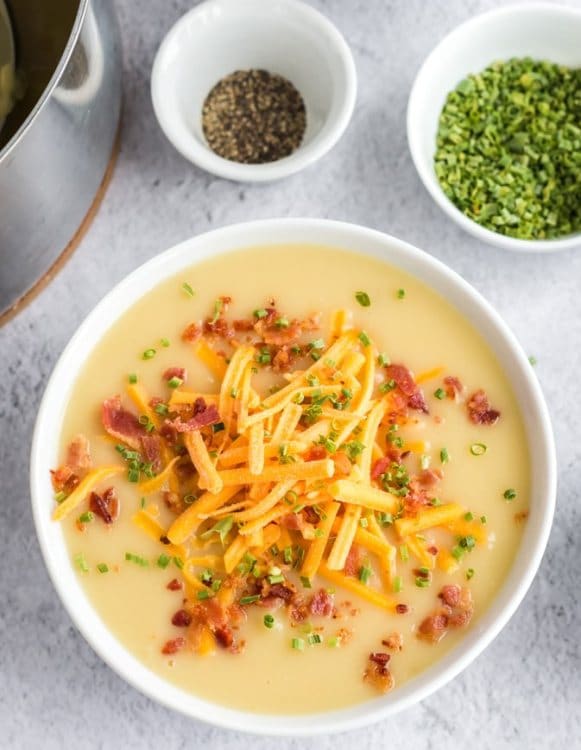 Cheese and potato soup topped with bacon bits, grated cheddar and chives