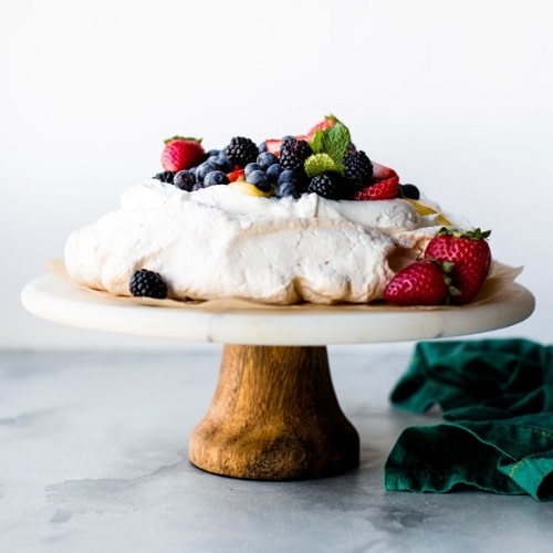 Baked Pavlova dessert on a wooden stand, decorated with fresh fruit.