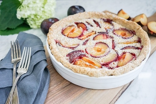 French cake with plums, served in a white baking dish.