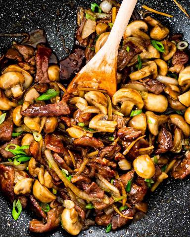 Beef in a minute with mushrooms and vegetables with a wooden spoon.