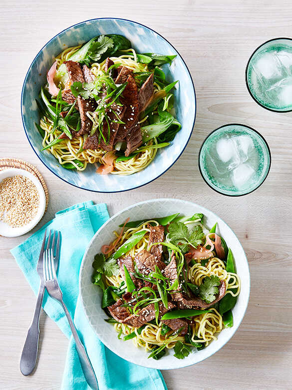Beef teriyaki with noodles, peas and bok choy on plates with forks.
