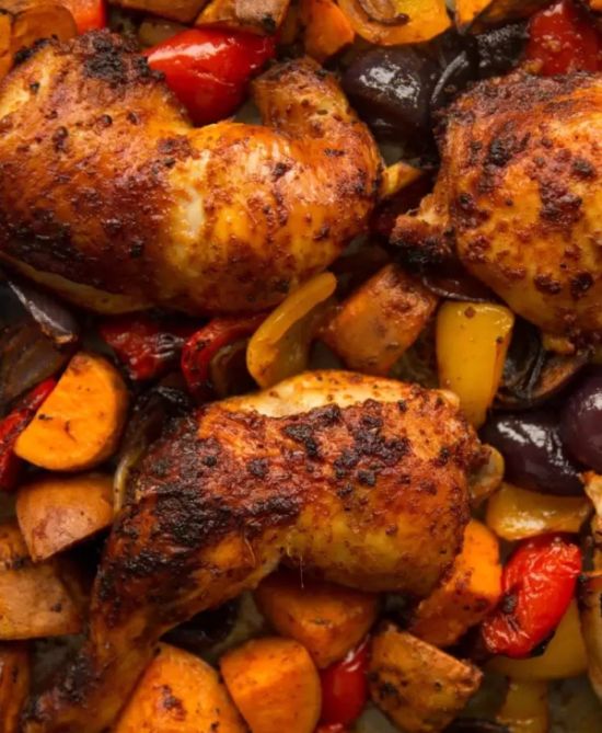 Pieces of chicken prepared on a baking sheet together with potatoes, peppers, onions, carrots and garlic