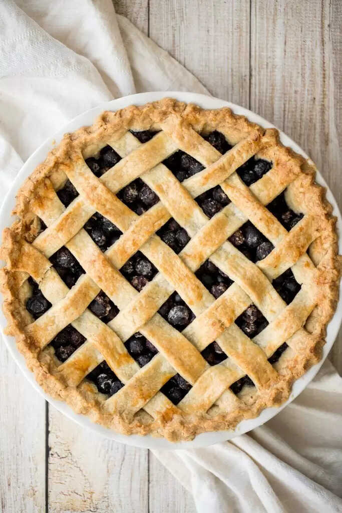 Blueberry pie decorated with strips of dough on a plate.