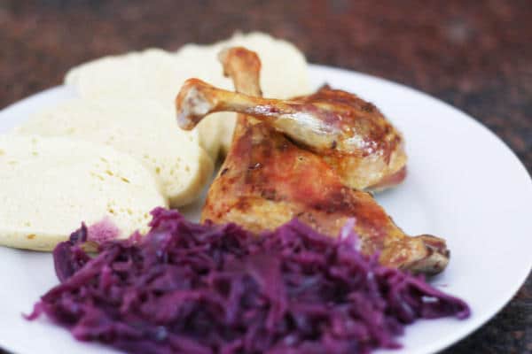Red cabbage with apples served with dumpling and duck on a white plate.