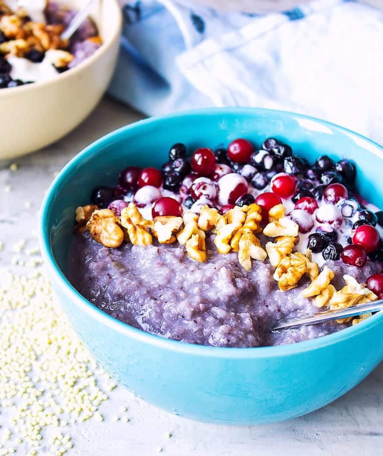 Millet porridge with blueberries, other fruits and walnuts in a blue bowl.