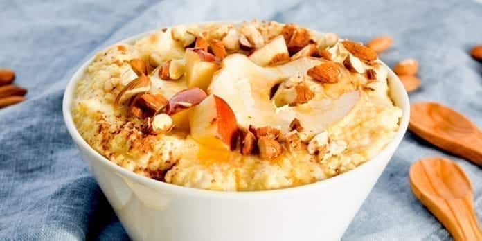 Millet pudding with apples in a bowl with wooden spoons next to it.