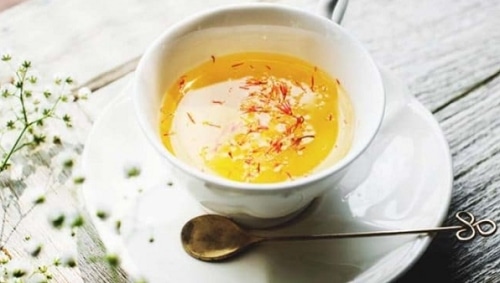 Čaj z pampelišky v bílém šálku s talířkem, zdobený čerstvými kvítky. 