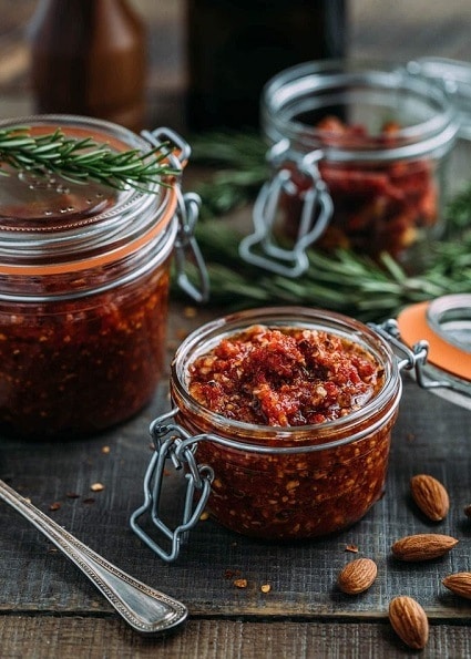 Sun-dried tomato pesto with almonds in a jar, garnished with a fresh sprig of rosemary.