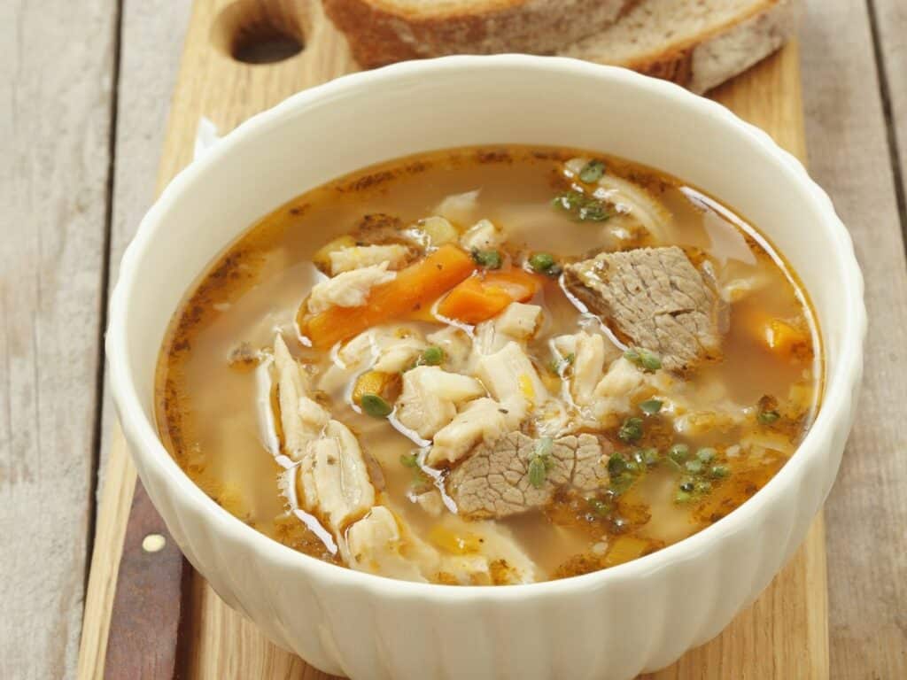 Klare Suppe mit Kutteln, Fleisch und Gemüse in einer weißen Schüssel.