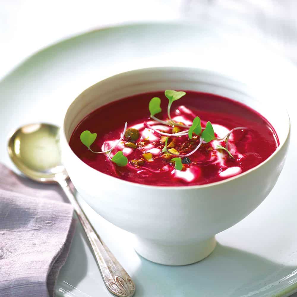 Spicy beetroot soup garnished with pea shoots served in a bowl with a spoon.
