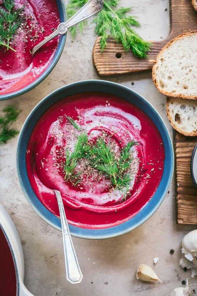 Creamy beet soup with dill served in a bowl with a spoon.