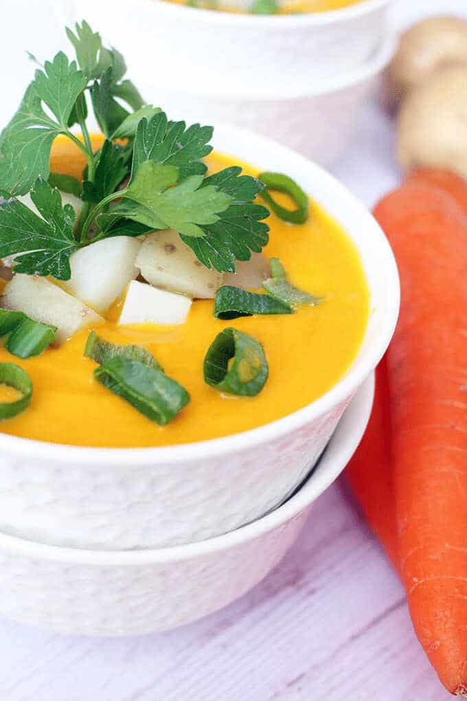 Creamy potato and carrot soup in a bowl sprinkled with spring onion and parsley.