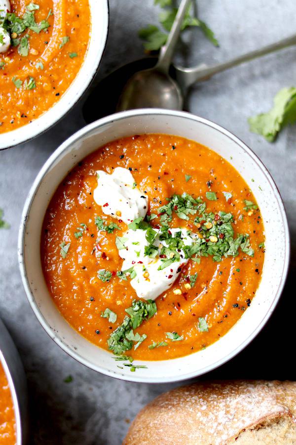 Spicy carrot soup with red lentils served in a bowl and garnished with herbs and yogurt.