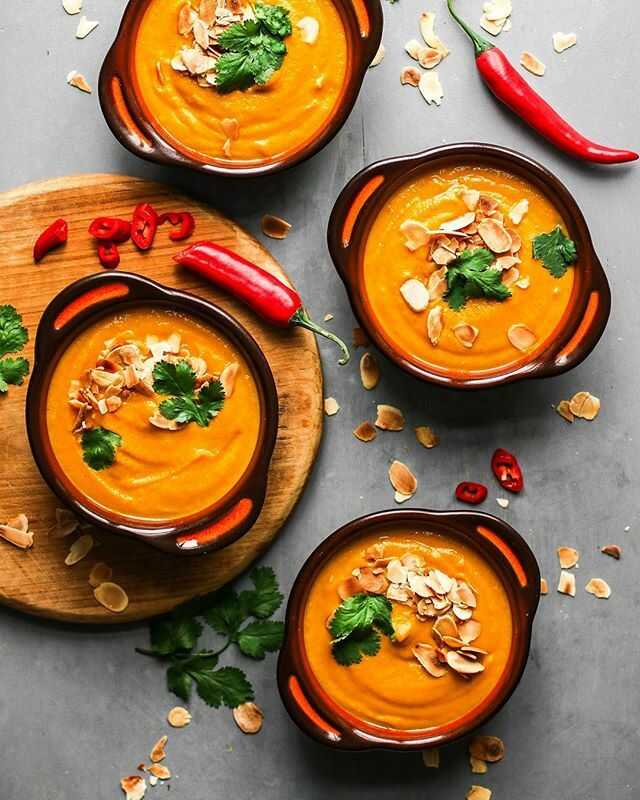 Spiced cauliflower and carrot vegetable soup garnished with almonds and herbs, served in bowls.