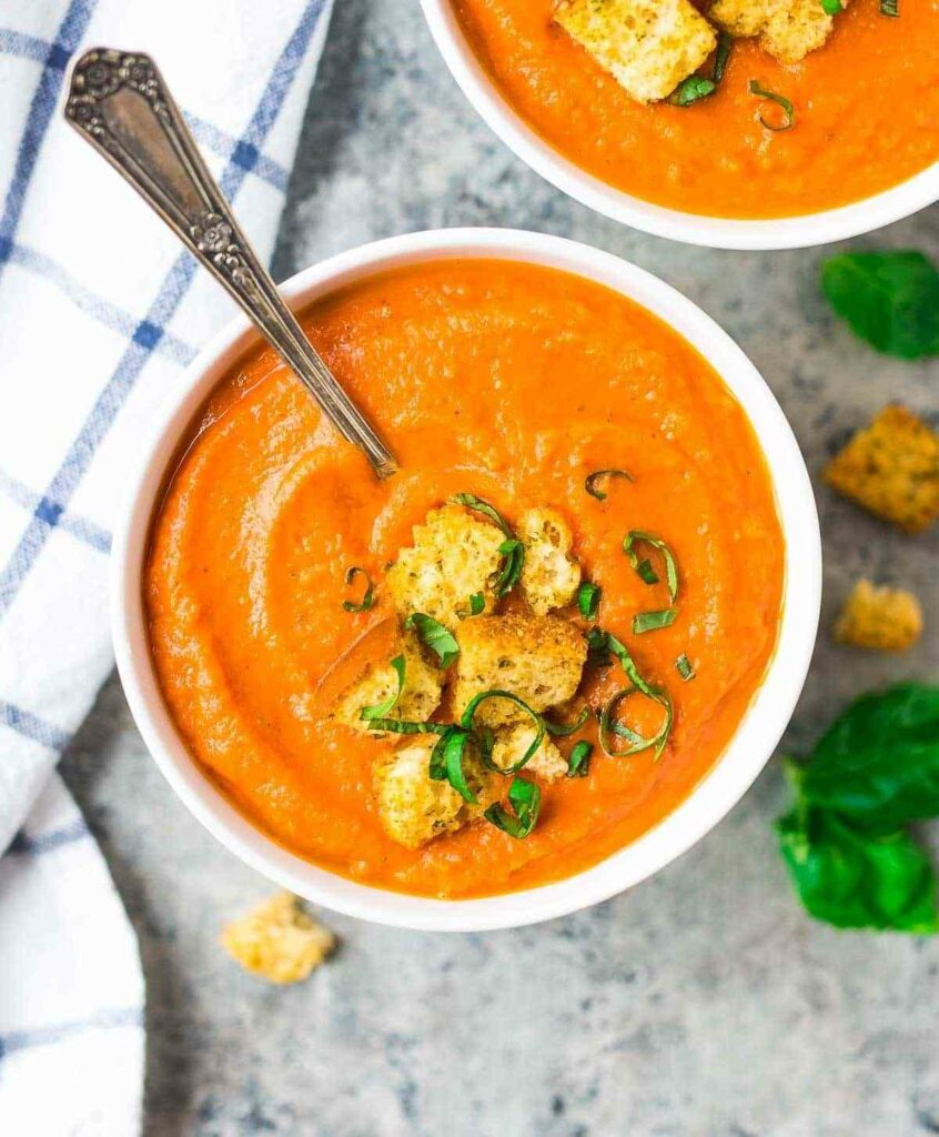 Roasted vegetable and tomato soup in a bowl decorated with croutons and herbs.