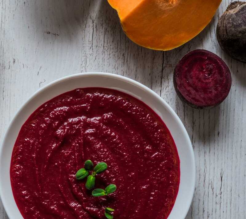 Vegetable soup served on a plate, with pumpkin and beetroot placed next to it.