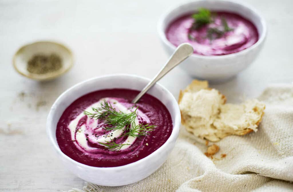 Beet soup with horseradish in a bowl decorated with dill and cream.