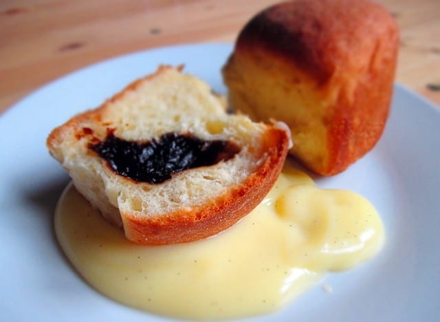 A halved bun filled with plums served on a plate with vanilla pudding.