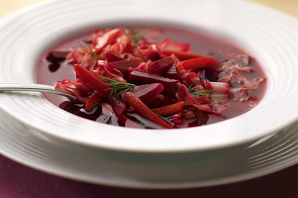 Beet soup with vegetables garnished with dill on a plate with a spoon.